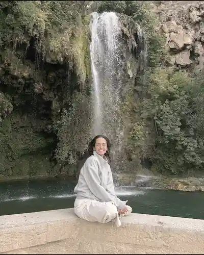 Clarisse assise en tailleur sur un muret, devant une cascade